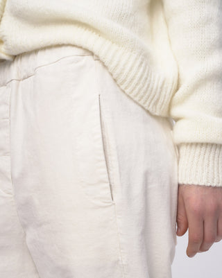 Close-up of a person wearing a white sweater and light-colored pants.