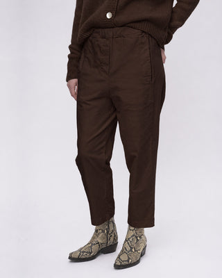 A person wearing dark brown cropped trousers with a ribbed knit sweater and snakeskin-patterned ankle boots, shown from the chest down against a light gray studio background.