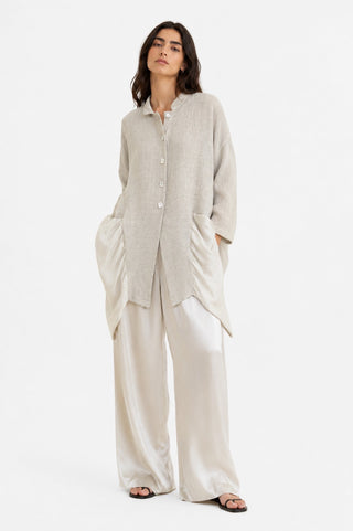 Woman wearing a beige button-up shirt and wide-leg pants on a white background