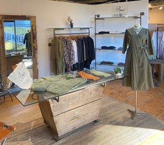Retail store interior with clothing on display, including a green dress and sweaters.
