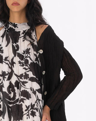 Woman wearing a black and white floral dress with a black cardigan on a white background