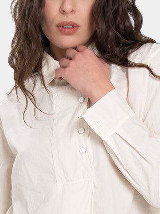 a close up photo of a model in a cream colored outfit with brown hair standing against a white background
