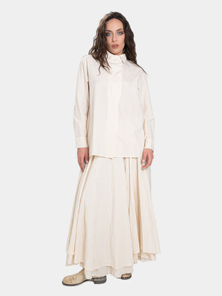 a model in a cream colored outfit with brown hair standing against a white background