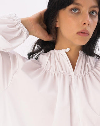 a model standing against a white background with a white blouse on.