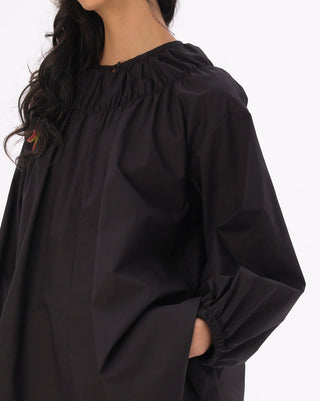 a model standing against a white background with a black blouse on. 