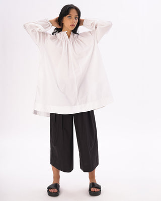 a model standing against a white background with a black and white outfit on. 