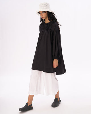 a model standing against a white background with a white hat and a black and white outfit on. 