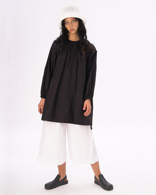 a model standing against a white background with a white hat and a black and white outfit on. 