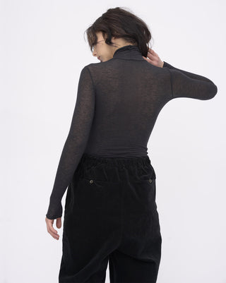 Person wearing a dark long-sleeve top and black pants on a white background