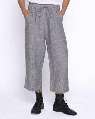 A person wearing loose, wide-leg gray cropped pants with a drawstring waist, paired with black lace-up boots against a plain white studio background.