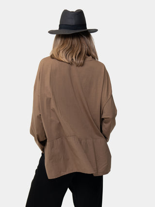 the back of a model wearing a black and brown outfit with a black hat, against a white background.