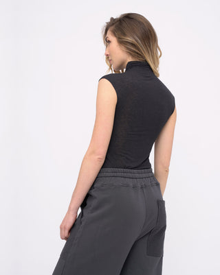 Woman wearing a black sleeveless top and gray pants on a white background