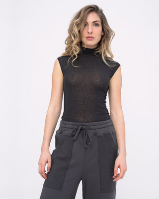 Woman wearing a black sleeveless top and dark pants on a white background