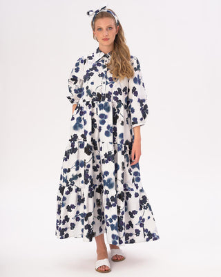 A woman wearing a floral tiered cotton belt maxi shirtdress with 3/4 length sleeves and white sandals. She has a headband on and the dress has a higher hemline.