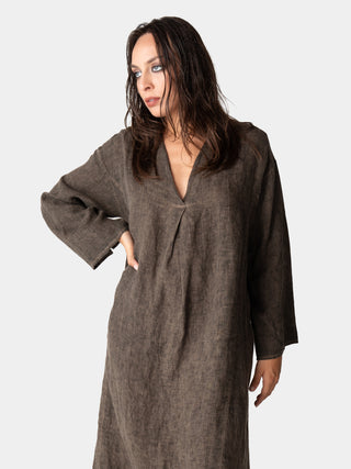 A model wearing a full-length beige linen kaftan dress with a V-neck and loose sleeves, paired with dark grey shoes.