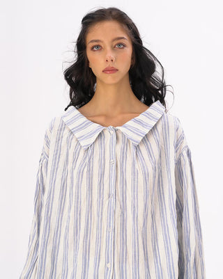 A model wearing a striped crinkled button up peasant shirt with a loose fit against a white background