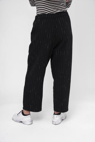 Person wearing black pinstripe pants and a striped shirt on a white background