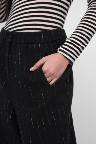 Person wearing a black and white striped shirt with black pinstripe pants on a plain background