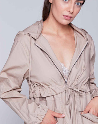 Woman wearing a beige trench coat with a white lace top underneath on a light gray background