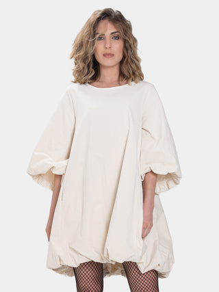 a model wearing a cream colored balloon dress in front of a white background