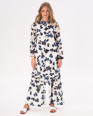 A woman modeling a white hi-lo floral button shirtdress with long sleeves and side slits.