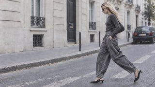 A woman walks across a city street crosswalk wearing a dark gray long-sleeve top and matching wide-leg corduroy trousers with black pointed-toe heels.