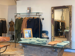 Clothing store interior with racks of clothes, a mirror, and a table with folded clothes.