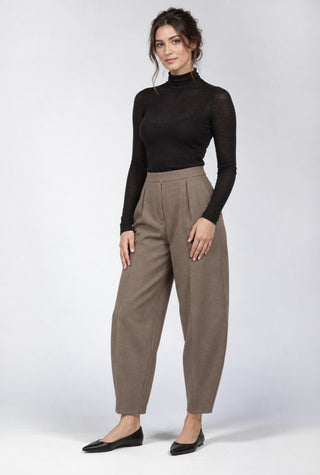 a brunette model against a light grey background wearing a black sweater and brown pants with black flat shoes.