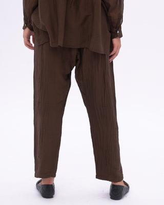 A person standing wearing brown cotton silk blend drawstring pants with an elastic waistband, tapered hem, and pockets.