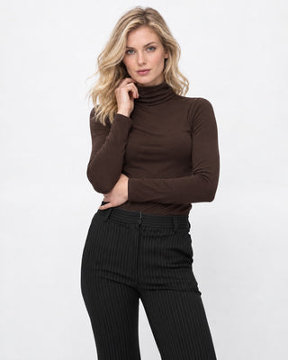 a blonde model wearing a brown turtleneck and black pin stripe pants against a white background