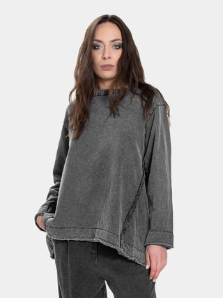 A woman modeling a washed charcoal gray long-sleeve top with a raw, frayed hem and a dark gray corduroy collar, paired with dark gray pants, against a light gray background.