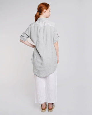 A female model wearing a button-up linen tunic with a mixed pattern of stripes and polka dots, paired with white wide-leg drawstring trousers.