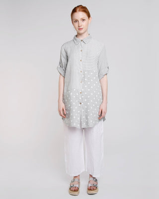 A female model wearing a button-up linen tunic with a mixed pattern of stripes and polka dots, paired with white wide-leg drawstring trousers.