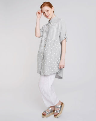 A female model wearing a button-up linen tunic with a mixed pattern of stripes and polka dots, paired with white wide-leg drawstring trousers.