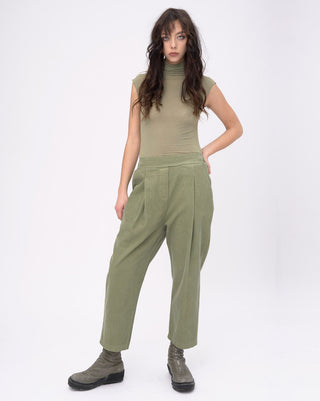 Woman wearing a green sleeveless top and high-waisted pants on a white background