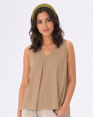 A woman wearing a sleeveless V-neck top in a light tan/beige color, paired with a matching olive green headband and light beige pants, set against a plain white studio background.