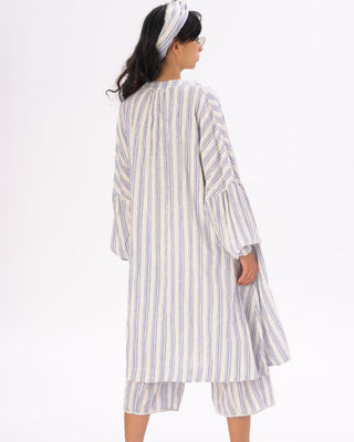 A female model wearing a striped cotton-linen duster in white and blue, with a headband, and matching shorts.