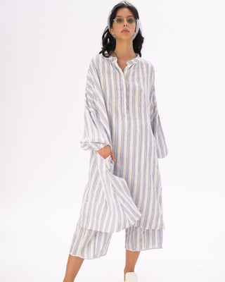 A female model wearing a striped cotton-linen duster in white and blue, with a headband, and matching shorts.
