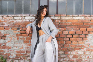 Woman in gray cardigan and black top leaning against a brick wall