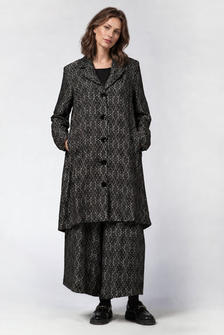 a brunette model standing against a white background wearing a dark grey geometric printed outfit. 