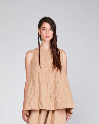 A female model wearing a beige crinkled crewneck tank top with a single pleat in the back.