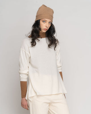 A female model wearing a beige rolled cuffed crewneck sweater with long sleeves and a brown hat.