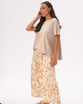 Woman wearing a beige top and patterned skirt on a white background