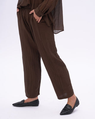 A person standing wearing brown cotton silk blend drawstring pants with an elastic waistband, tapered hem, and pockets.
