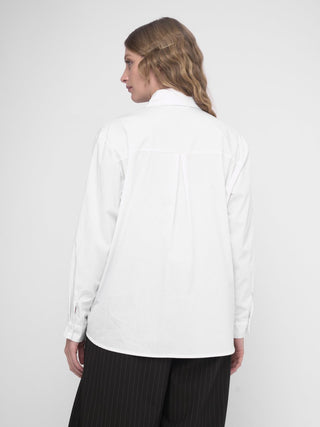 A woman wearing a white buttoned long sleeve shirt with a layered crop shirt over the top, paired with a dark skirt.