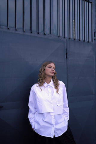 A woman wearing a white buttoned long sleeve shirt with a layered crop shirt over the top, paired with a dark skirt.
