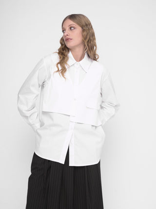 A woman wearing a white buttoned long sleeve shirt with a layered crop shirt over the top, paired with a dark skirt.