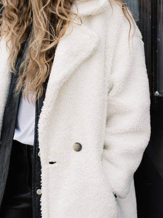 a close up of a model with blonde hair wearing a white overcoat. 