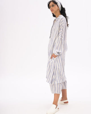 A female model wearing a striped cotton-linen duster in white and blue, with a headband, and matching shorts.
