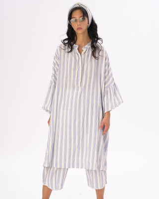 A female model wearing a striped cotton-linen duster in white and blue, with a headband, and matching shorts.